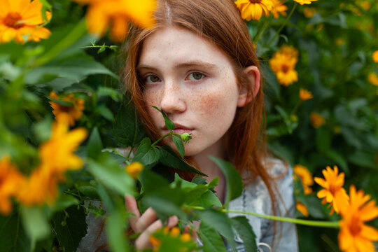 Portrait with red hair and freckle among yellow flower in summer