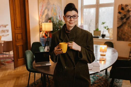 Entrepreneur standing in warm home office holding yellow mug