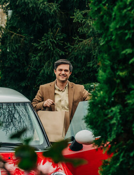 Smiling shopper arriving home with paper bags by a red car