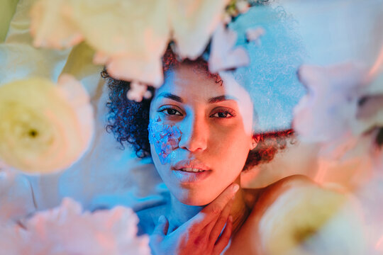 Beautiful woman lying behind glass surface with flowers under neon lights