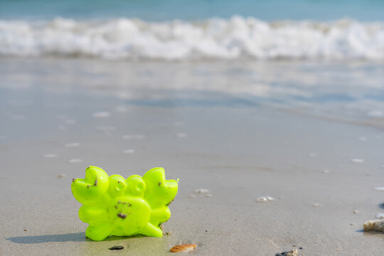 Seaside Crab Toy on Sandy Shoreline: A vibrant green crab toy sits on a sandy shoreline with gentle waves in the background, a playful scene of summer leisure and beachside fun.