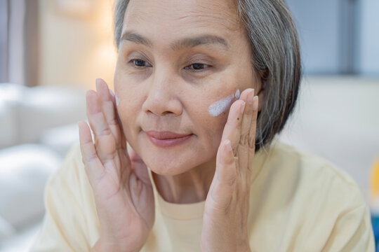 Close-up mature Asian woman applying nourishing antiage face skin care cream treatment