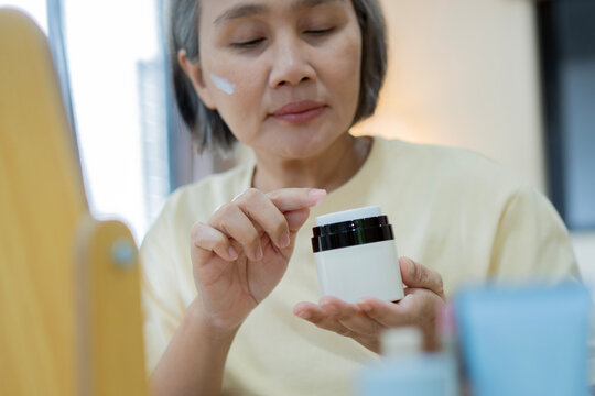 Beautiful mature Asian old woman applying skincare product to face in a beauty routine