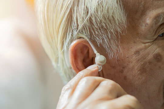 Close-up of a gray-haired senior man using his hearing aid in his ear with copy space