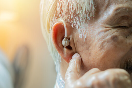 Close-up of a senior man with hearing aid and pointing finger to his ear