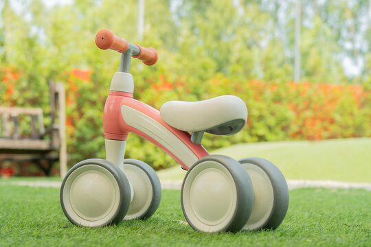 Cute pastel orange and beige plastic childrens tricycle with handlebars at outdoor park