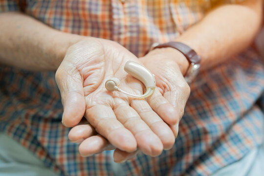 Close-up senior man wearing plaid shirt holding of an electronic hearing aid in his hands.