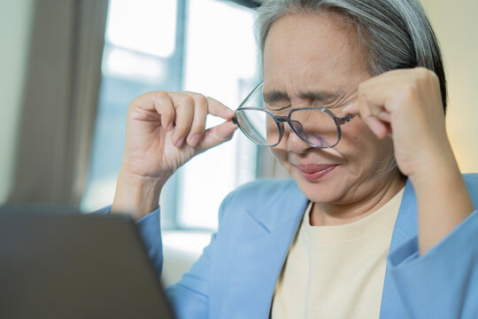 Mature woman feels headache and stress while working on laptop at home office.