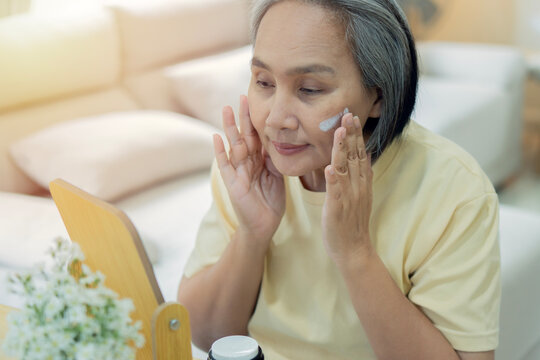 Happy mature person with cosmetics application for glowing face in home.