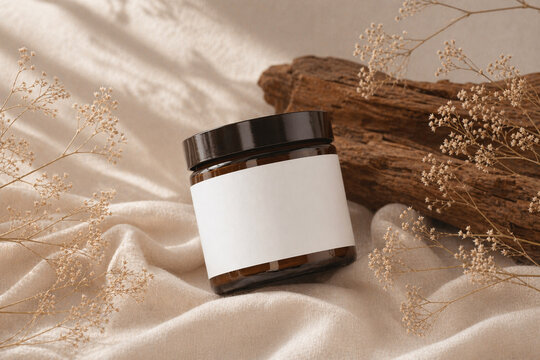Blank amber glass jar mockup on beige fabric with dried flowers and natural light