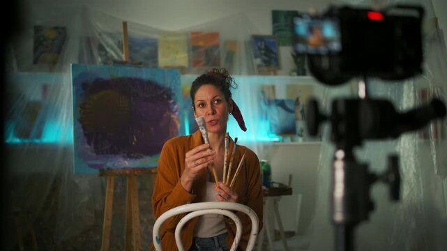 Female artist recording an online painting workshop or tutorial in her creative studio.