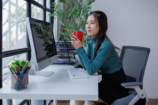 Asian woman taking coffee break at modern office desk