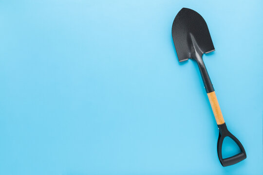 New dark black metal gardening shovel for little child on light blue table background. Pastel color. Closeup. Empty place for text. Top down view.
