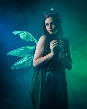 close up portrait of female model wearing fantasy fairy costume, green dress, butterfly wings and crown. standing pose holding  magical glass orb.  glowing green  lighting, dark studio background