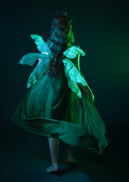 portrait of female model wearing fantasy fairy costume, green dress, cloak, butterfly wings and crown. full length standing pose, holding  magical crystal orb.  isolated on dark studio background.