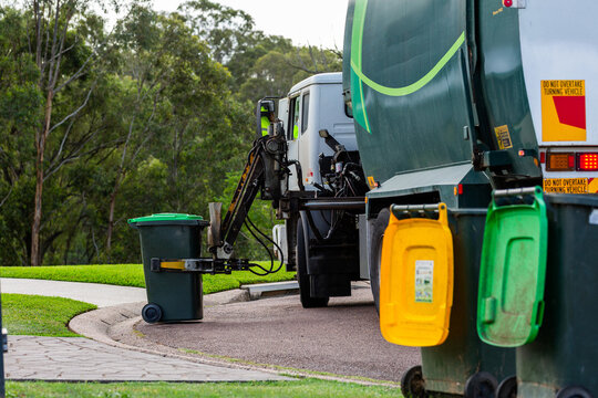 Streetscape scene of garbage truck emptying green fogo bin on urban street