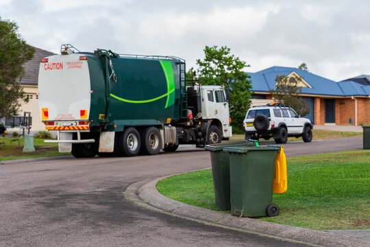 Streetscape scene of garbage truck emptying green fogo bin on urban street