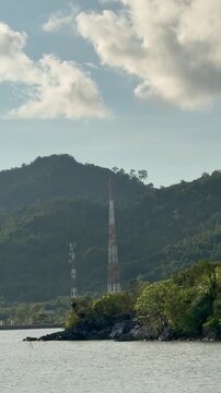 Two cell towers stand on a small island surrounded by water with mountains.