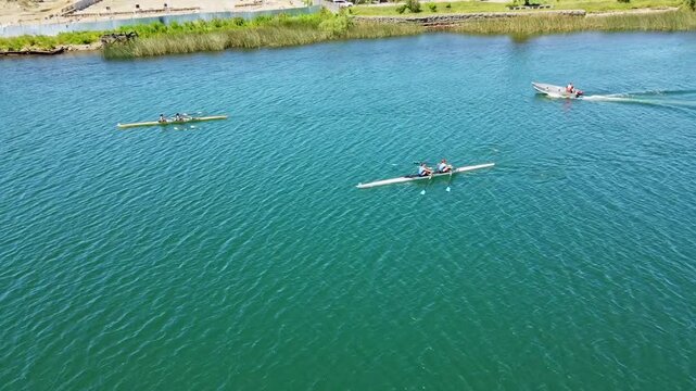 Aerial view of a rowing team in a long racing boat moving swiftly across blue water.