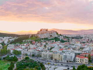 Naklejka premium Acropolis and parthenon defining the skyline, providing a view of athens city buildings, streets, and mountains during a colorful sunset, depicting ancient history merging with modern life