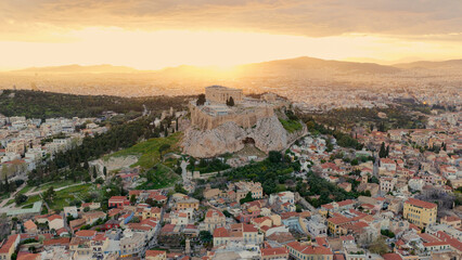 Obraz premium Ancient parthenon ruins crown the acropolis rock, overlooking athens as the setting sun bathes the cityscape in warm golden light, highlighting historic architecture and urban sprawl