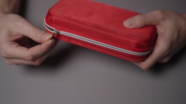 Person hands opening and closing red first aid kit with zipper, showing emergency medical equipment for health, safety and accident preparedness in closeup. Shooting in slow motion.