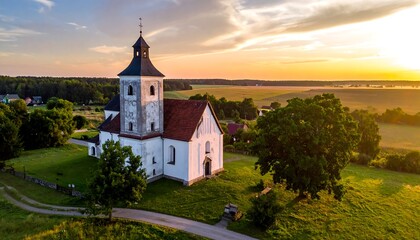 Naklejka premium Scenic drone view of church with tower in green landscape, sunset sky