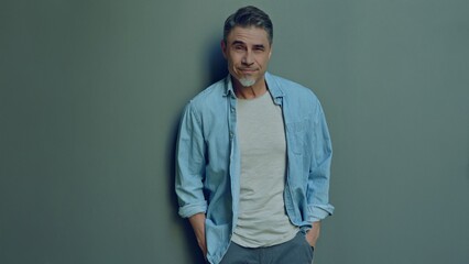 Obraz premium Portrait of a relaxed man in 50s wearing casual denim shirt. Confident happy male smiling. Blank copy space for text on grey wall background.