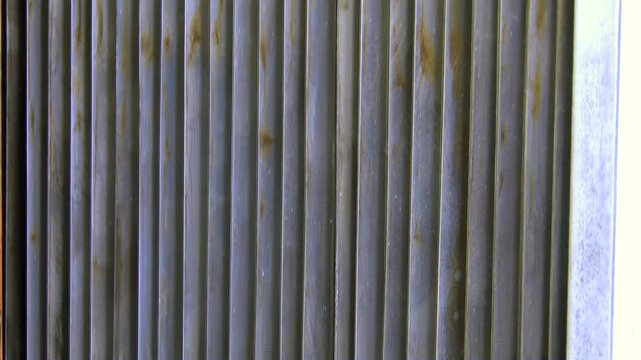 A metallic bar glides with steady rhythm across a wall of vertically ribbed, industrial panels. Hints of rust adorn the textured surface, showcasing the machine's relentless work during the day.