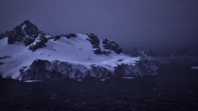 wide sweep of antarctic ice coast under moody dusk sky, low angle captures massif silhouette, distant icebergs and rough sea convey remoteness and scale