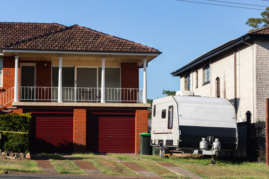 Caravan parked beside driveway outside brick home with red roller garage doors