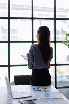 Businesswoman standing by window planning future strategy