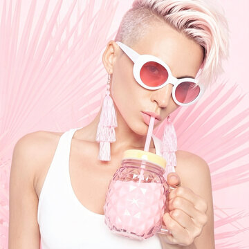 Stylish woman with pink undercut hair drinking summer cocktail from pineapple jar on pastel background