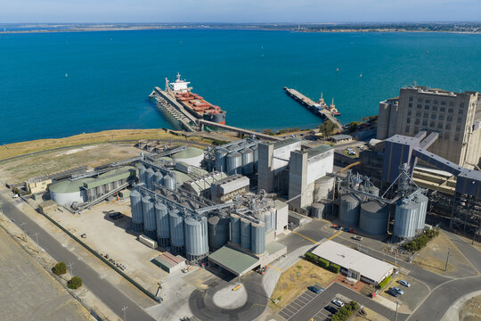 Aerial view of a cargo ship at a port with storage tanks and silos