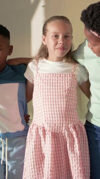 Vertical video: Speaking center girl making peers lean and laugh for fun in room in pink gingham