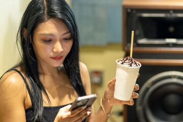 Young woman relaxing with a smartphone and drink in a trendy Bangkok audiophile cafe