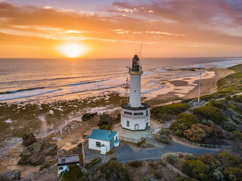 Aerial view of golden sunset over a lighthouse on a coastal cliff