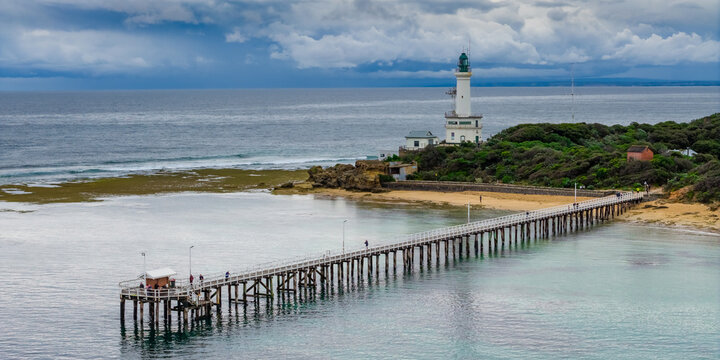 Aerial view of storm clouds approaching a coastal lighthouse and long narrow jetty over a calm bay