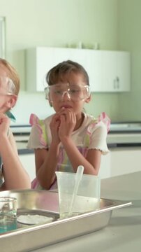 Right-side student adjusting goggles, leaning and observing experiment with beaker in science class