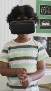 Reaching youth wearing black VR headset tapping, rotating controls at desk striped tee math poster
