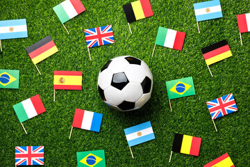 Classic soccer ball surrounded by small flags of different countries on green grass, creating a world cup vibe. International football championship concept. Top view, flat lay. © PixelArt_25