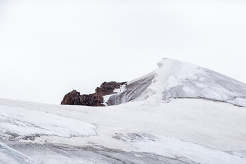 Detailed view of a snow-covered mountain crest with a dangerous snow cornice against a clean white sky in Almaty region. © Roman
