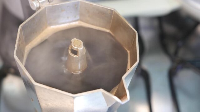 Close-up of intense steam swirling and rising from a moka pot. A boiling Italian coffee maker steaming on a stovetop. POV: brewing fresh espresso coffee. Hot black coffee brewing in a moka pot. 