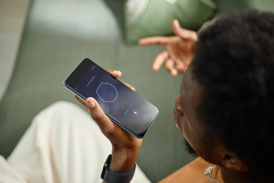 Black young adult man using smartphone voice assistant, speaking command and gesturing during hands free mobile interaction. Useful for app marketing, smart tech ads, close up