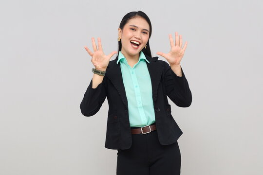 A young Asian woman stands smiling looking at the camera, raising her hand and showing nine fingers explaining rules, numbers, or steps, isolated on a white background.