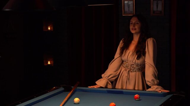 Beautiful woman playing billiards and dancing around the pool table with her friend. Young ladies having fun and celebrating in a nightclub with snooker. Nightlife, active leisure, and friendship.