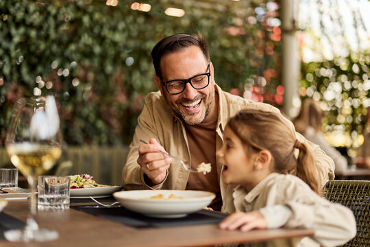 Father Feeding Daughter and Laughing Together at Outdoor Restaurant Dining Table