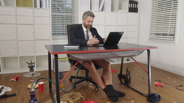 Funny business man laughing at office mess. Comic remote office full of chaos. Freelancer man working in a funny messy space. Business humor in a crazy home workplace.
