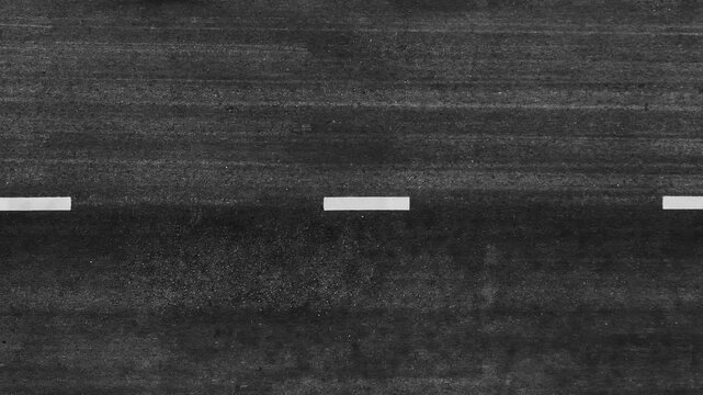 High-angle aerial image of a dark asphalt roadway with lane markings, highlighting travel, progress, connectivity, infrastructure planning, movement, simplicity, and urban development concepts. 4k.
