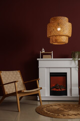 Naklejka premium Interior of stylish living room with cozy armchair, fireplace and glowing lamp near red wall